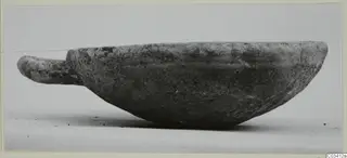 Hand-made pottery bowl with a short horizontal handle, shown in side view against a pale background.
