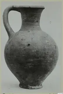 Pottery Plain White Wheel-made jug from Enkomi, with a single loop handle and tall neck, shown against a grey backdrop