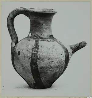 Wheel-made pottery juglet with a high loop handle, a side spout and two dark painted bands on a pale body.