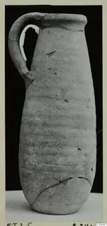 Tall narrow-necked jug with a single strap handle, photographed against a dark background.