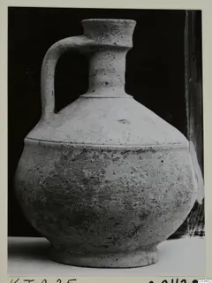 Single-handled jug with a narrow neck and flared rim, photographed against a black background.