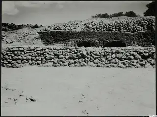 Temenos wall at Ayia Irini with a rubble-topped earth bank behind it, low hills and trees beyond