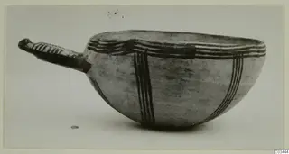 Bowl with a long handle and dark painted bands on a pale surface, photographed in side view