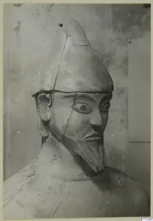 Terracotta statue from Ayia Irini with a tall conical headdress, large eyes and a long beard, seen from the chest up