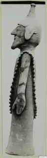 Terracotta figurine in side profile, standing, with a long neck, prominent nose and rows of applied knobs down the sides.