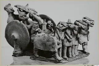 Terracotta group of standing figures and a quadruped beside a large upright disc, on a rectangular base