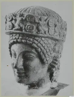 Limestone head of a statue from Arsos, wearing a tall carved headdress with a fluted top and braided hair