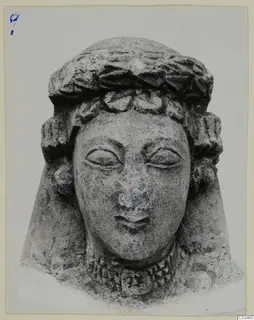 Limestone head sculpture with a wreath-like headband and curled side locks, photographed face-on