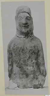 Standing limestone statue of a figure with a cap-like headdress, photographed from the front