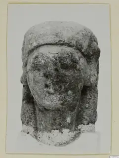 Limestone sculpture of a head with a tall headdress and worn face, seen from the front.