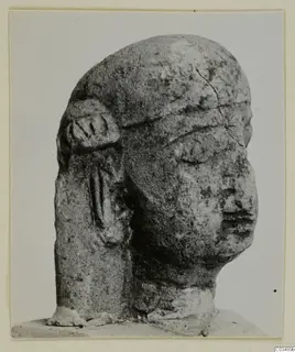 Limestone sculpture of a human head with a worn face and a carved ear-like form on the left side