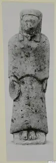 Limestone statue of a standing figure in a long robe and close head covering, hands at the body, on a rectangular base