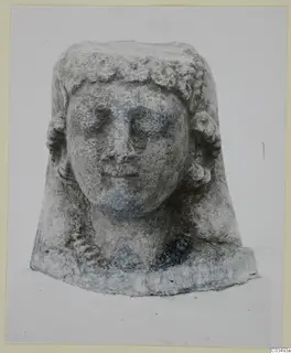 Limestone sculpture of a head with curled hair and a flat-topped crown, shown from the front