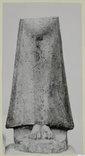 Limestone sculpture of a tapering figure with two carved feet at the base, photographed against a plain grey background.