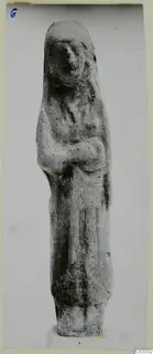 Terracotta figurine of a standing figure with a covered head and arms held across the body