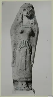 Standing female figure in grey relief, with a rounded top, raised breasts and a long garment, on a stepped base