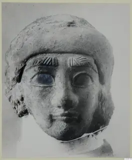 Terracotta head of a figure in a rounded cap, with hatched eyebrows and large eyes, photographed frontally.