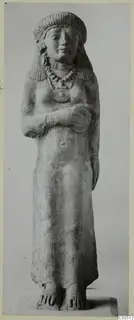 Standing female terracotta figure with arms folded across her chest, wearing a bead necklace and pendant.