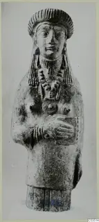 Terracotta figurine of a standing figure with a tall headdress and arms folded across the chest