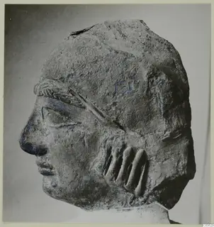 Terracotta head in left profile, with a banded headband and ridged locks of hair at the side.