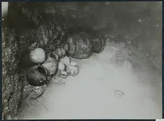 Pots and bowls lying against a rock face during excavation