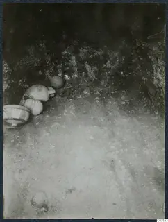 Pottery vessels lying on the sandy floor of an excavation at Stylli, against a rough rock wall.