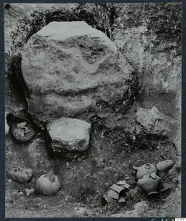 Excavation at Stylli with several broken pots and objects lying on the excavated floor beside a large stone