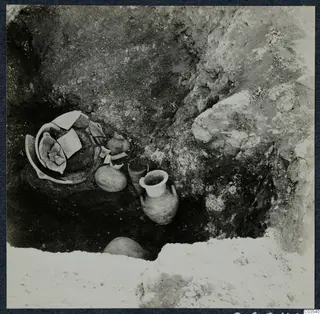 Excavation at Stylli with pottery vessels and broken sherds lying in the soil of a pit.