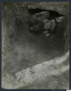 Excavation at Stylli showing a cut with a dark opening in the rock wall, partly blocked by a heap of stones