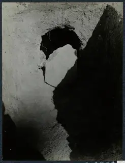 Excavation at Stylli with a large stone slab leaning in front of a dark opening cut into earth