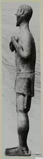 Side view of a standing bearded terracotta statue with hands held at the chest