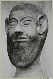Terracotta head of a bearded man with large ears and almond-shaped eyes, shown against a pale background