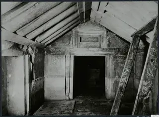 Interior of a built tomb chamber with sloping stone roof slabs, wooden props and graffiti on the walls