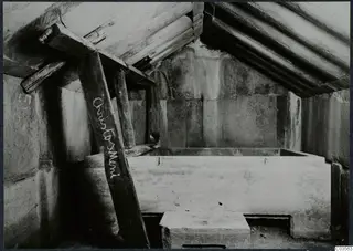 Built tomb chamber with timber props under a sloping roof and a large rectangular stone block in the centre.