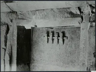 Interior of a built tomb chamber with scratched graffiti on stone slabs, cracks, and a dark opening to one side.