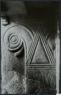 Close view of carved stone with a spiral scroll at left and a triangle outlined by raised parallel bands at right