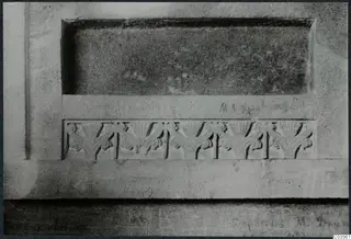 Close view of carved stone with a row of five fan-shaped reliefs below a recessed panel and faint lettering.