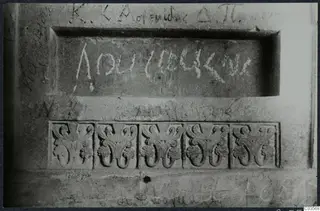 Carved stone wall in a built tomb chamber, with a recessed inscribed panel, five relief ornaments below and scratched graffiti