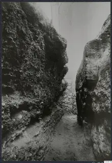 Narrow passage between tall rock faces, with a built stone wall at its far end