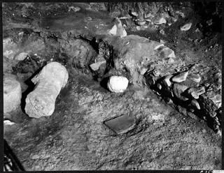 Finds in situ during excavation at Cholades, Soli: a cylindrical stone block, a rounded stone and a flat slab in the ground.