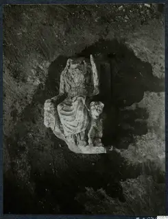 Seated draped stone statue lying in excavated soil at Cholades, Soli, with a smaller carved figure beside it.