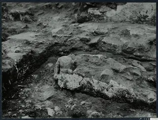 Carved stone figure fragment lying in excavated soil among stone blocks at Cholades, Soli.