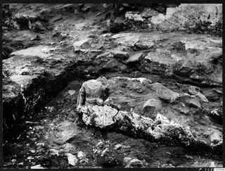 Excavated trench at Cholades, Soli, with a partly uncovered figure in pale stone lying among stones and soil