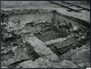 Excavation at Soli showing a stone wall and paved stone features in a trench, with a railway line at the top edge