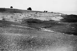 Excavated temple remains at Soli on a grassy hillside, with a small tent beside the ruins and the sea beyond.