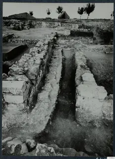 Excavated stone walls and a narrow trench at Cholades, Soli, with a tent and trees on the skyline behind.