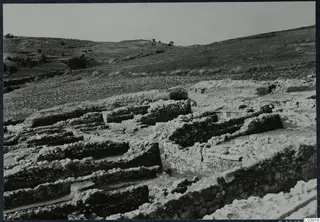 Excavated stone walls and foundations at Soli, Cholades, with a grassy hillside and trees behind.