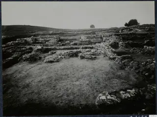 Stone wall foundations of Soli's Cholades temples across a cleared excavation area, with a low hill behind