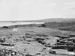 Excavated stone walls at Soli with a white tent, and a bay with a ship and small boats beyond