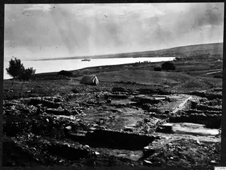 Excavated walls at Soli with a tent on the slope and a small boat on the bay below